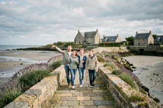 Famille en balade sur le passage submersible de Saint-Cado en Bretagne, avec les maisons en granit et l'estuaire en arrière-plan